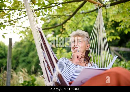 Portrait von glücklichen Senior Frau sitzen im Freien auf Hängesessel im Garten, entspannend. Stockfoto
