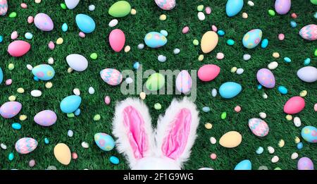 Helle und bunte Ostereier und Süßigkeiten mit rosa Hasenohren Stockfoto