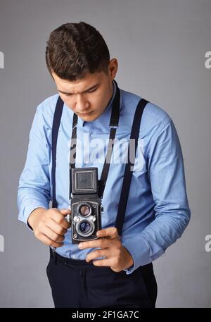 Schöner und stilvoller Mann in blauem Hemd und Hosenträger machen Foto auf alten Vintage-Kamera Stockfoto