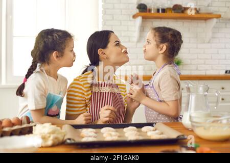 Verspielte Mama und Töchter machen Kekse und haben Spaß beim Schnurrbart aus Teig. Stockfoto