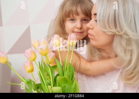 Kleine Mädchen von kaukasischen Aussehen gratulieren ihrer Mutter auf Mutter Tag und geben Sie einen Blumenstrauß und zärtlich Umarmungen In einem hellen Wohnzimmer Stockfoto