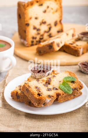 Hausgemachter Kuchen mit Rosinen, getrocknetem Kaki und einer Tasse heißer Schokolade auf grauem Betonboden und Leinentextilien. Seitenansicht, Nahaufnahme, selektiv Stockfoto