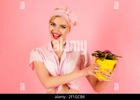 Lächelnde Frau mit violetter Blume im Topf. Mädchen, das Blumen kultiviert. Bepflanzung. Stockfoto