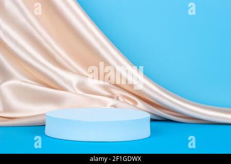 Geometrische Podium auf hellblauem Hintergrund mit drapierten Champagner Farbe Seidenstoff. Schaufenster für Produktpräsentation Stockfoto