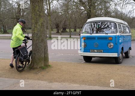 Mann Radfahrer in gelb hohe Sichtbarkeit Jacke Park Fahrrad Agains Ein Baum neben VOLKSWAGEN WOHNWAGEN in blau und Weiß in London Greenwich Park Stockfoto