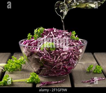 Veganes Konzept, gesunde Ernährung. Rotkohlsalat wird mit Olivenöl auf schwarzem Hintergrund gegossen, in einem rustikalen Stil, geringe Tiefenschärfe, selektiv Stockfoto