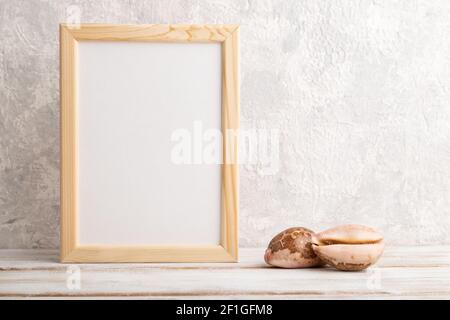 Weißer Holzrahmen-Mockup mit Muscheln auf grauem Beton-Hintergrund. Leer, vertikale Ausrichtung, Standzeit, Kopierraum. Stockfoto