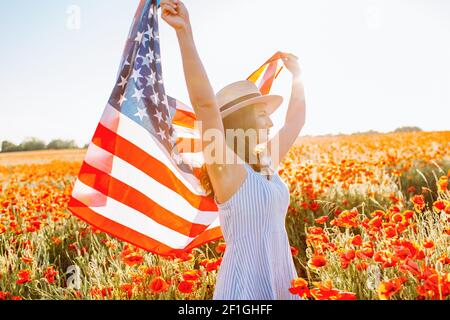 Frau im Sommerkleid und Hut mit winkender Flagge der Vereinigten Staaten in Mohn Feld an klaren sonnigen Tag. Unabhängigkeitstag, nationales Feiertagskonzept Stockfoto