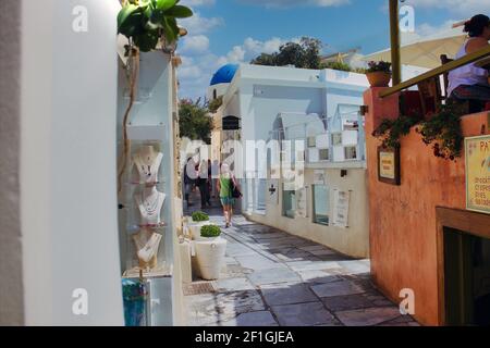 Santorini, Griechenland - 11. September 2017: Eine schmale Handelsstraße mit Juweliergeschäft auf der linken Seite, Touristen zu Fuß in der Mitte und Menschen sitzen in Stockfoto