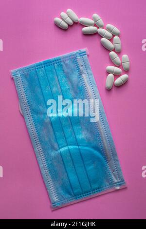 Medizinische blaue Schutzmaske und weiße Tabletten, Kapseln, Pillen oder Vitamine auf einem rosa Hintergrund Stockfoto