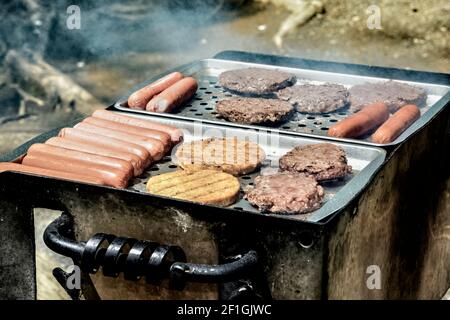 Horizontale Aufnahme von Burgern und Hot Dogs, die auf einem Grill im Freien kochen. Stockfoto