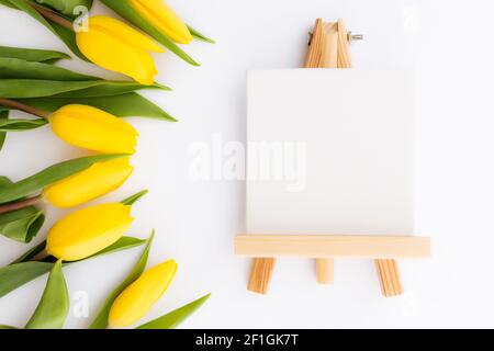 Flaches Lay mit gelben Tulpenblüten, leerer Bilderrahmen auf weißem Hintergrund. Konzept für Grußkarte für Ostern, Muttertag, Internationale Frauen Stockfoto