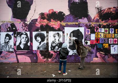 Madrid, Spanien. März 2021, 8th. Eine Frau zeigt ihrem Sohn ein feministisches Wandbild, das heute während des Internationalen Frauentags verwüstet erschien. Plakate von Frauen wurden über die Gemälde gelegt, nachdem das Wandbild mit schwarzer Farbe zerstört wurde. Das Wandbild zeigt berühmte Frauen aus der ganzen Welt, mit den Gesichtern von 15 Frauen, die Teil der Geschichte für ihren Kampf für die Gleichheit sind: Kredit: Marcos del Mazo/Alamy Live News Stockfoto