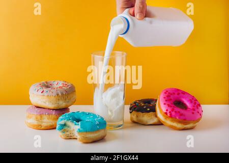 Bunte Donuts mit Schokolade, Erdnussbutter und Marmelade Füllung. Man Hand gießt Pflanzenmilch in das Glas. Sweet Tooth Home Frühstück für Text-Kopie Stockfoto