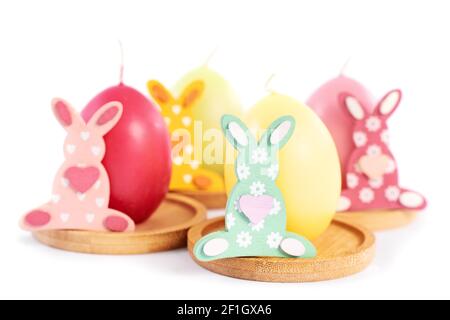 Nahaufnahme von kleinen Osterhasen neben eiförmigen Kerzen in Pastellfarben, isoliert auf weißem Hintergrund. Witziges, farbenfrohes Osterfest-Konzept. Stockfoto