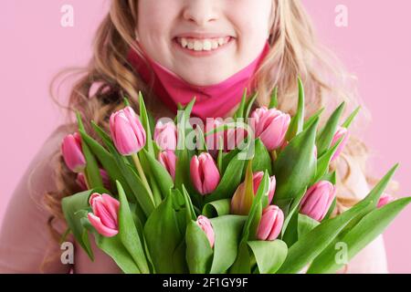 Nahaufnahme auf glückliches Kind mit Tulpenstrauß und rosa Maske isoliert auf rosa. Stockfoto