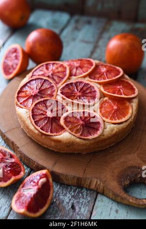 Hausgemachter Obstkuchen. Blutorangenkuchen mit rohen Bio-Orangen auf Eichenbrett vertikal Stockfoto