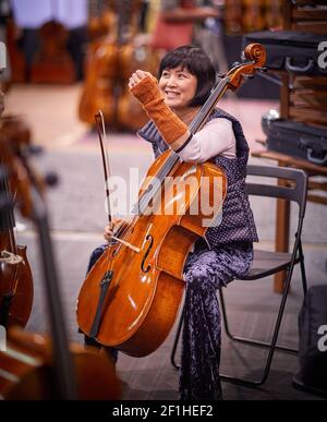 Asiatische Frau lächelnd und eine Pause vom Spielen Cello Mit Korsett am Handgelenk bei der Musical Instrument Convention Stockfoto