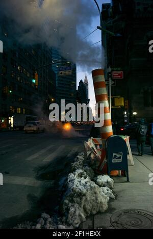 Dämmerung in New York City an einem verschneiten Tag. Eine Dampfleitung und das Chrysler Building, Stockfoto