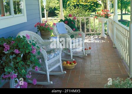 Wicker Schaukelstühle auf einer gemauerten Veranda mit blühenden Topfblumen - ein privater Ort, Missouri, USA Stockfoto