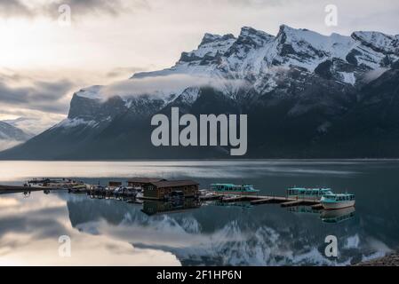 Morgennebel brennt von einem Spiegel noch Lake Minnewanka in Banff an einem frühen Junimorgen. Stockfoto