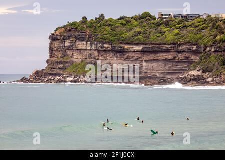 Surfer im Meer warten auf eine Welle in Avalon Strand in Sydney mit Häusern am Wasser im Hintergrund The Headland, Sydney, NSW, Australien Stockfoto