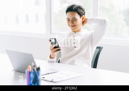 Asiatischer Geschäftsmann lehnt sich zurück in seinem Stuhl und mit Das Telefon während der Pause Stockfoto