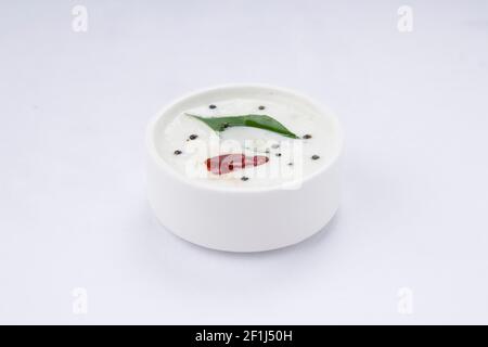 Coconut White Chutney, in einem weißen Tischgeschirr angeordnet und gewürzt mit Musterd, roter trockener Chili und Curryblättern. Stockfoto