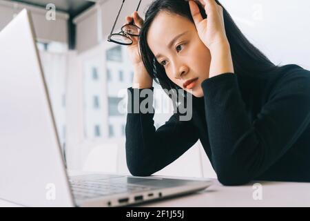 Bild von gestressten asiatischen Frau arbeiten von zu Hause auf Laptop suchen besorgt, müde und überwältigt Stockfoto