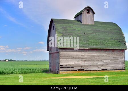 Malta, Illinois, USA. Ein Veteran Scheune sitzt allein zwischen den weiten offenen Raum des ländlichen Illinois unter Windturbinen und Kulturen. Stockfoto