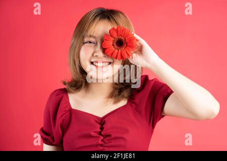 Das junge Mädchen hielt eine rote Gerbera Blume, die eine bedeckte Auge Stockfoto