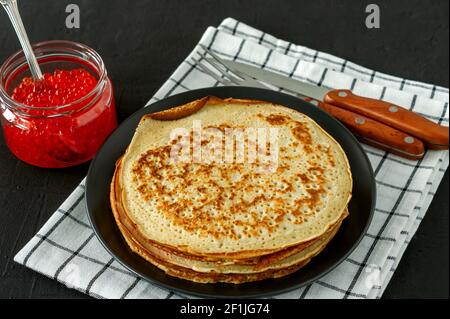 Traditionelle russische Crepes Blini in einem Teller mit rotem Kaviar auf Holzgrund gestapelt. Maslenitsa traditionelles russisches Festmahl. Russische Küche, Stockfoto