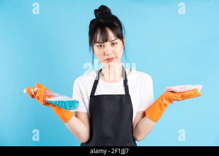 Asiatische Hausfrau trägt orange Handschuhe und hält ein Spray Von Wasser in ihrer Hand Stockfoto