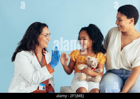 Arzt gibt hoch fünf Mädchen sitzen mit ihrer Mutter in der Klinik. Mädchen Besuch Arzt mit ihrer Mutter für die Untersuchung. Stockfoto