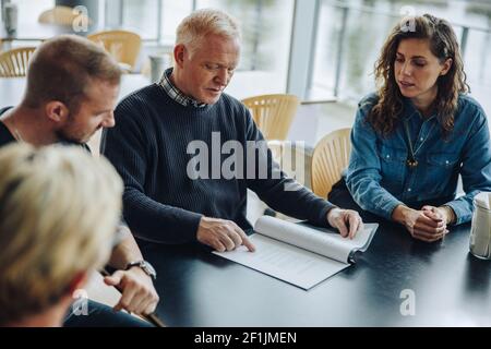 Leitender Mitarbeiter liest ein Vertragsdokument mit Kollegen, die im Sitzungssaal sitzen. Geschäftsteam diskutiert über einen Vertrag im Büro. Stockfoto