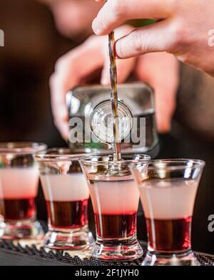 Rotes alkoholisches Getränk in Gläsern an der Bar. Roter Cocktail im Nachtclub. Barkeeper bereitet Cocktail-Shooter. Der Barkeeper gießt starkes alkoholisches Getränk hinein Stockfoto