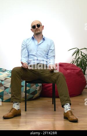 Baldheaded bärtig lässig trendy brutal kaukasischen cool Macho oder Gangster Mann in Sonnenbrille hält Rosenkranz auf Stuhl sitzen Blick auf Kamera. Co Stockfoto