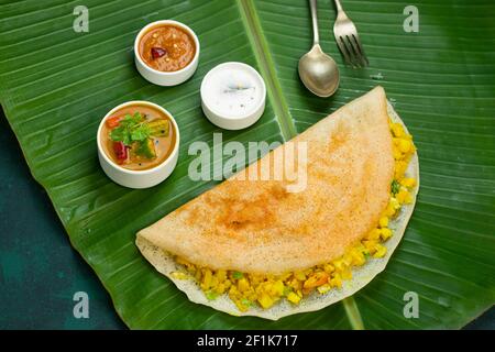 Dosa  Masala dosa, berühmtes südindisches Frühstückselement, das in einer Kasteneisernen Pfanne auf traditionelle Weise hergestellt und auf einem frischen Bananenblatt angeordnet wird. Stockfoto