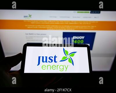 Person mit Mobiltelefon und Firmenlogo des kanadischen Energieunternehmens Just Energy Group Inc. Auf dem Bildschirm vor der Webseite. Konzentrieren Sie sich auf die Telefonanzeige. Stockfoto