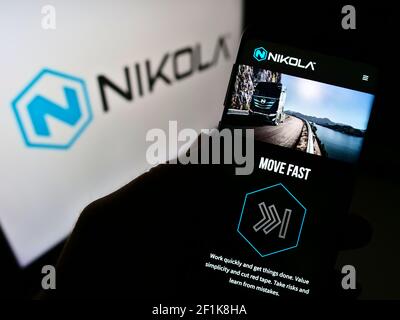 Person, die Mobiltelefon mit der Webseite des US-amerikanischen Elektrofahrzeugunternehmens Nikola Corporation auf dem Bildschirm vor dem Logo hält. Fokus auf der Mitte des Telefondisplays. Stockfoto