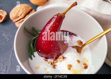 Schüssel mit süß pochierter Birne in Rotwein und Eis auf dunklem Hintergrund, Nahaufnahme Stockfoto