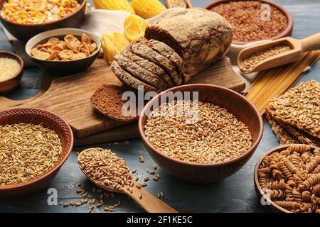 Verschiedene Cerealien, rohe Pasta und Brot auf farbigem Holzhintergrund, Nahaufnahme Stockfoto