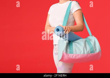 Junge Frau mit Sporttasche und Yogamatte auf Farbe Hintergrund Stockfoto