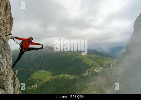 Attraktive junge Bergsteigerin auf einem Klettersteig in Die Dolomiten in einem verrückten Stretching Pos. Stockfoto