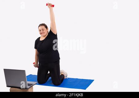 Übergewichtige junge kaukasische Frau macht Übungen zu Hause mit Online-Personal Trainer für die Gewichtsabnahme mit Hanteln. Ferntraining vor Stockfoto