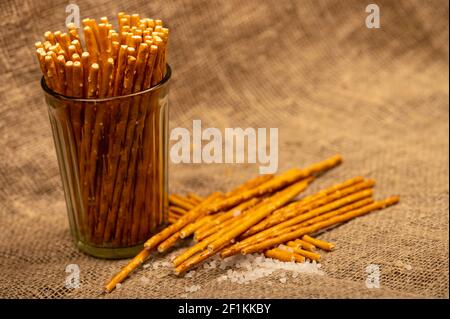 Salziges Brot Streifen in einer Glastasse und auf einem Hintergrund von groben homespun Stoff verstreut. Nahaufnahme, selektiver Fokus. Stockfoto