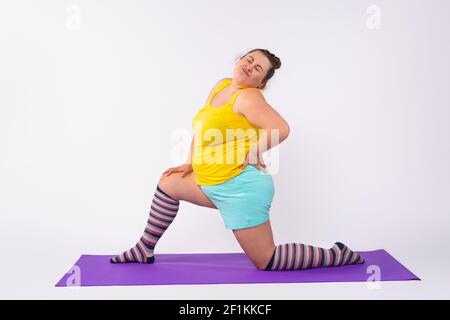In voller Länge eine junge, übergewichtige, kurvige Frau in der farbenfrohen Sportkleidung, die zu Hause auf einer Matte Yoga praktiziert. Entschlossenheit, Willenskraft, Sport Stockfoto