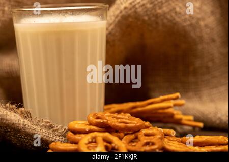 Gesalzene Brotstangen und gesalzene Brezeln in loser Schüttung und ein Glas Milch auf dem Tisch. Nahaufnahme mit selektivem Fokus. Stockfoto