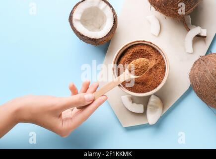 Frau hält Löffel von süßem Kokoszucker auf Farbhintergrund Stockfoto