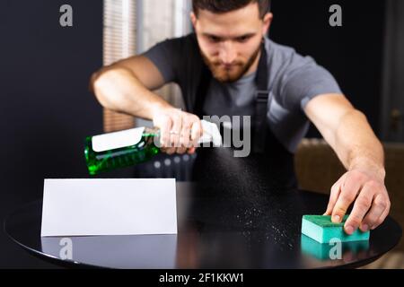 Konzept des Reinigungs- und Reinigungsservice. Lächelnder junger Mann, der Waschmittel verwendet, im Büro-Studio stehend, leerer Raum, weißer Leerraum für Text Stockfoto